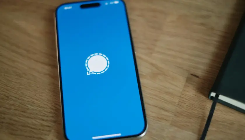 Telefon z niebieskim ekranem i ikoną komunikatora Signal. Obok leży czarny notatnik.