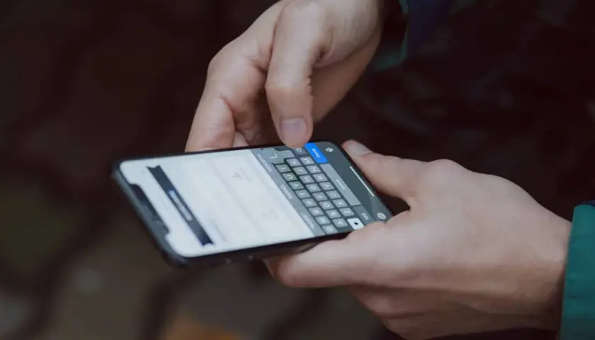 Dłonie trzymające smartfon z klawiaturą. Widoczna opcja "jak zwiększyć litery w telefonie" na ekranie.