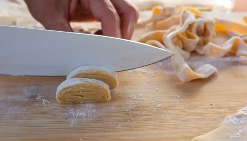 Eine Hand schneidet mit einem Messer frisch gerollte Teigrollen, um Makkaroni selber zu machen.