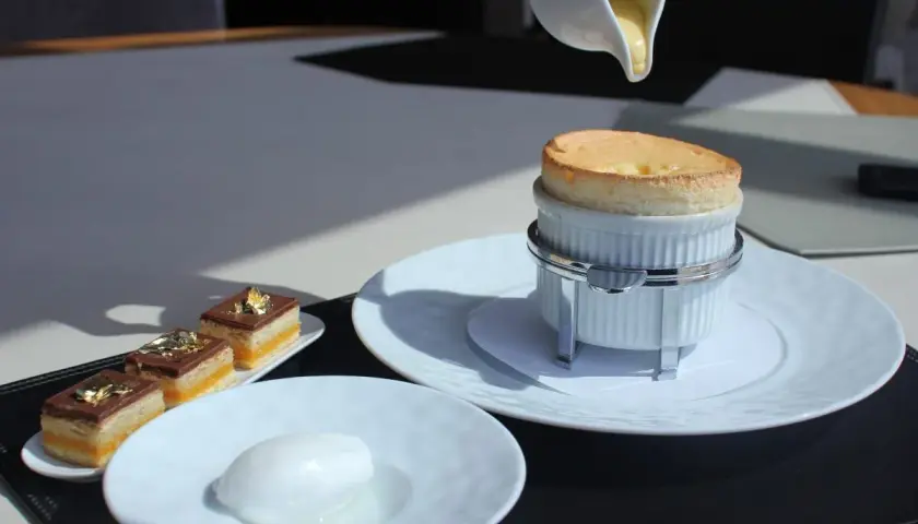 Un délicieux soufflé au Grand Marnier, encore chaud, est servi avec une crème anglaise. À côté, des petits gâteaux au chocolat et une boule de sorbet.