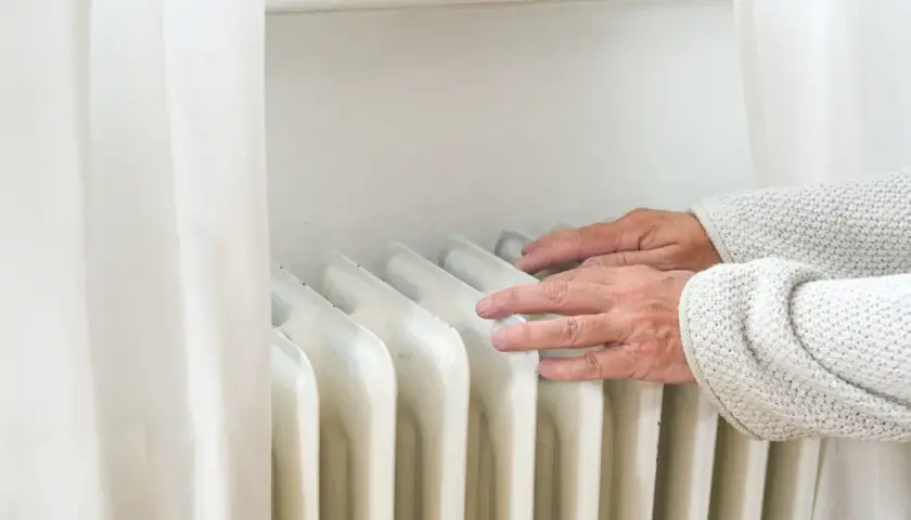 Dłonie sprawdzają temperaturę grzejnika, zastanawiając się, dlaczego grzejnik grzeje tylko do połowy.
