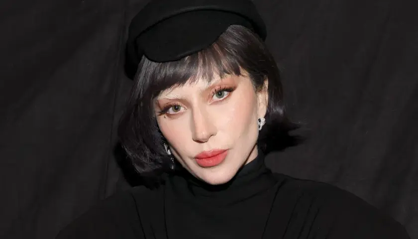 Lady Gaga w czarnym kapeluszu i golfie, z makijażem i biżuterią.