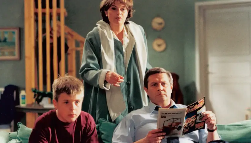 Familjen Svensson samlad i vardagsrummet. Pappa läser tidningen, mamma står och pratar, sonen sitter bredvid.