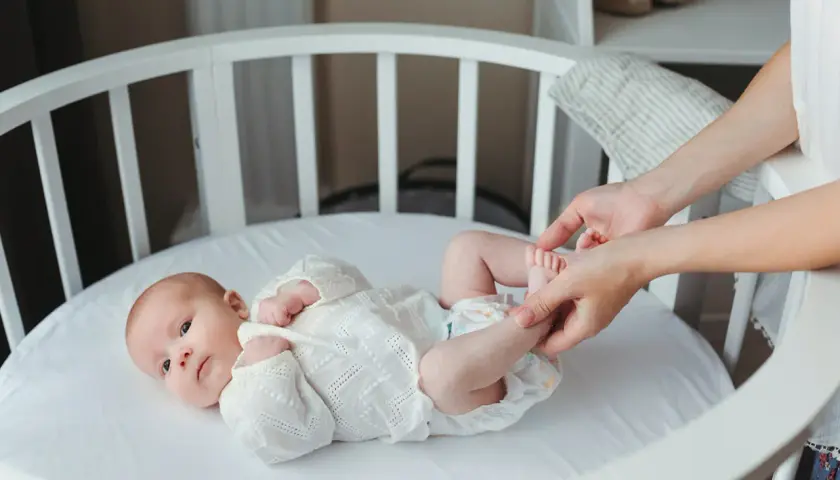 Delikatne nóżki noworodka w białej koronkowej kaftaniku, mama delikatnie je dotyka.