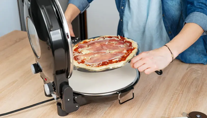 Osoba wkłada do pieca pizzę z szynką i serem. Już niedługo będzie można cieszyć się smakiem domowej pizzy.