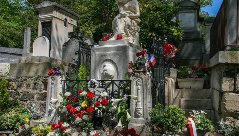Grób Chopina na cmentarzu Père Lachaise w Paryżu, ozdobiony kwiatami i flagami.