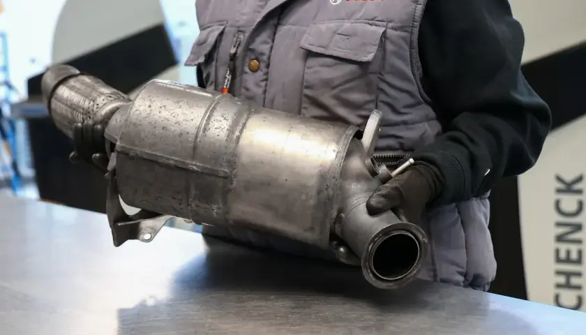 Mechanik w rękawiczkach trzyma element układu wydechowego. To część do diesla bez DPF, gotowa do montażu lub wymiany.