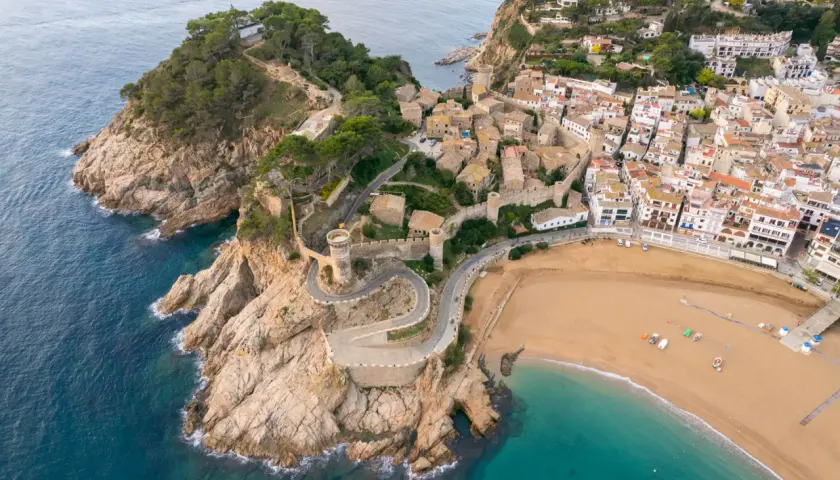 Widok z lotu ptaka na Tossa de Mar z kamiennymi murami obronnymi, wieżami i plażą.
