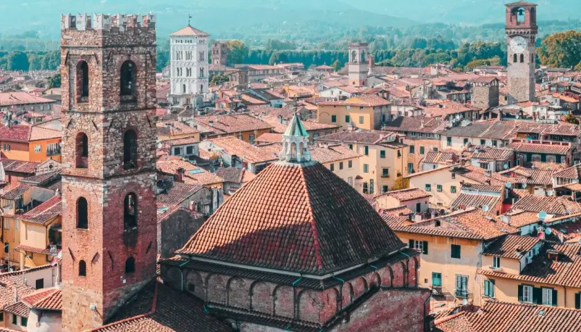 View over a walled city in Tuscany, with terracotta roofs, ancient towers, and distant mountains.