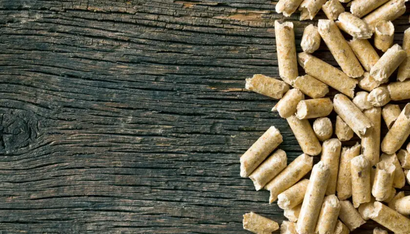 Drewniane deski i stos pelletu. Czy pellet jest ekologiczny? To pytanie zadaje sobie wielu, a ten obrazek pokazuje jego naturalne pochodzenie.