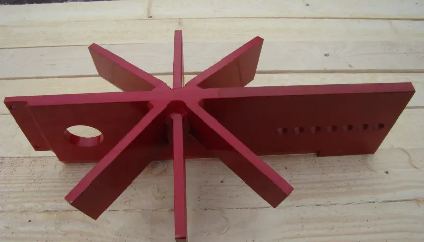 Rotes, sternförmiges Werkzeug mit acht Zacken, das wie ein spaltkreuz universal aussieht, liegt auf Holzbrettern.