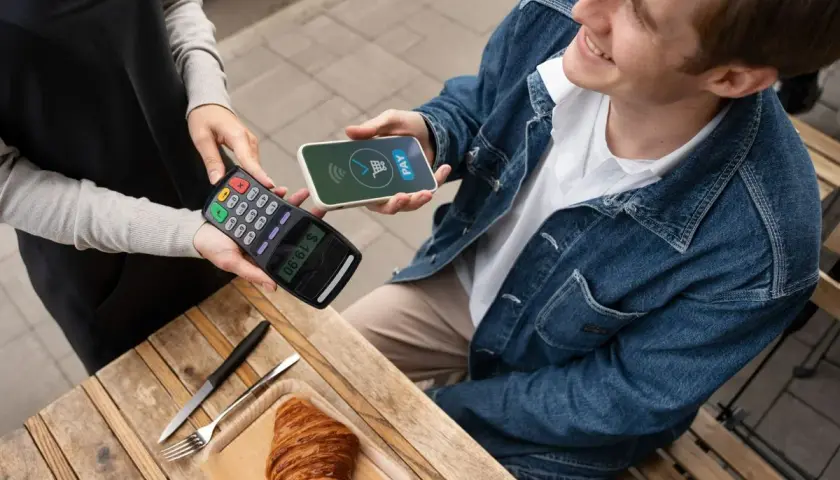Uśmiechnięty mężczyzna płaci telefonem Santander za croissant. Szybko i wygodnie, jak płacić telefonem Santander.