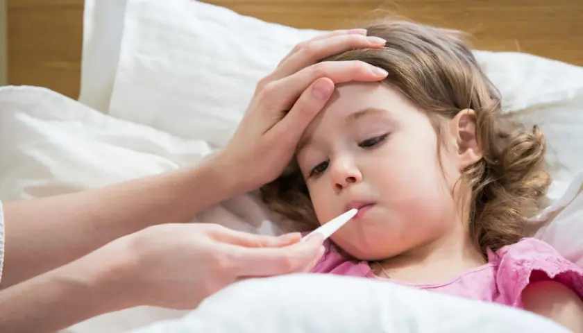 Bambina a letto con termometro in bocca, mano sulla fronte. La febbre da ansia la fa stare male.