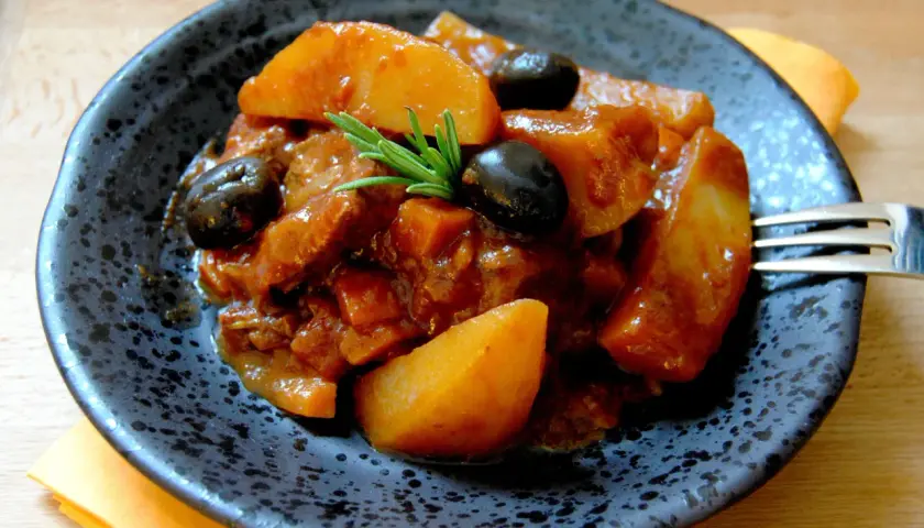 Un plat appétissant de sauté de veau à la tomate, garni d'olives noires et de romarin. Quel vin avec sauté de veau à la tomate ? Un rouge léger serait parfait.