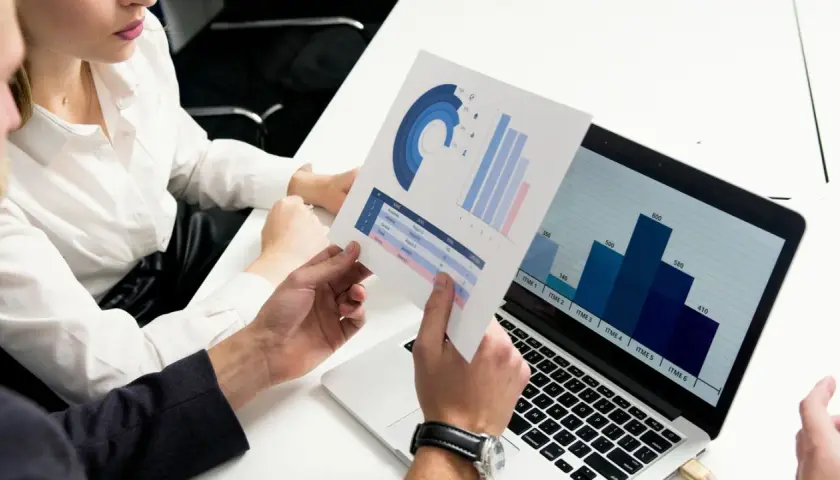Data scientist analizuje wykresy i dane na laptopie, omawiając wyniki z kolegą.