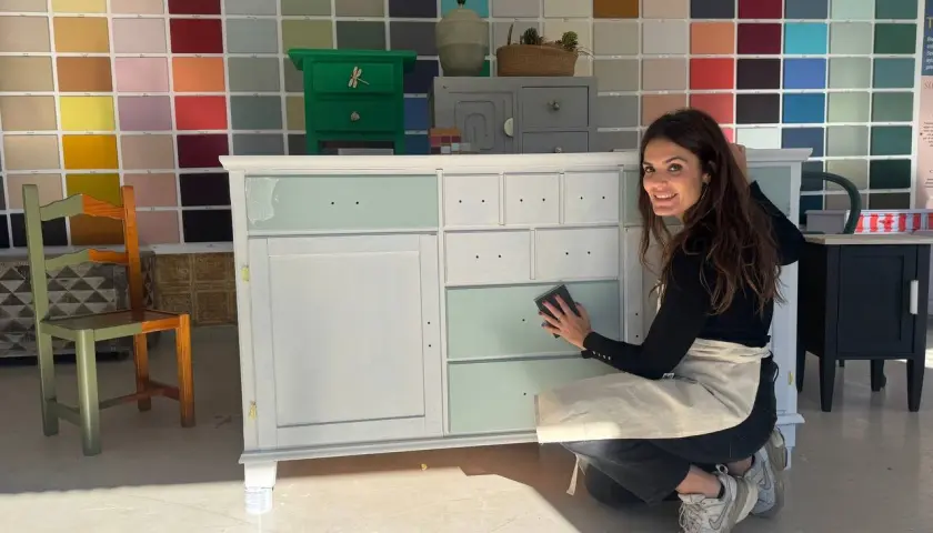 Mujer lijando un armario en proceso de pintura, con un fondo de muestras de colores.