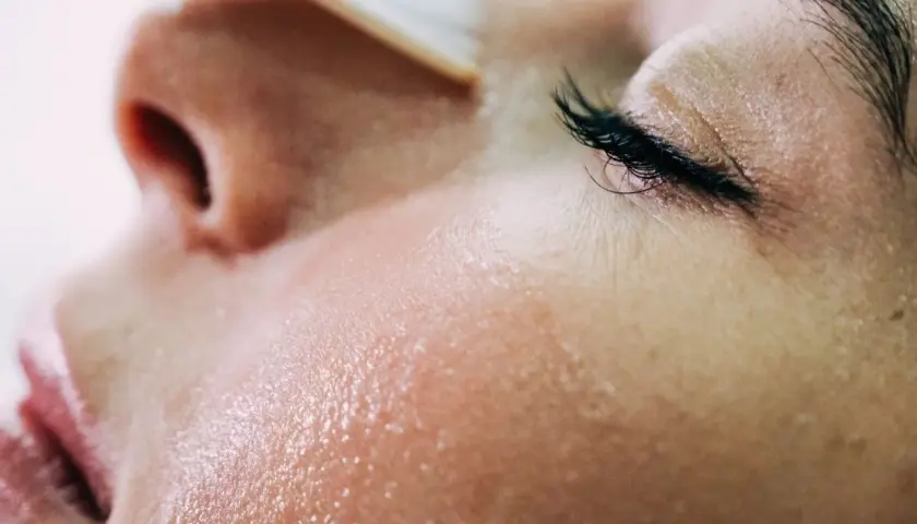 Gros plan sur une peau grêlée, humide et lumineuse, avec un œil fermé et des cils longs.