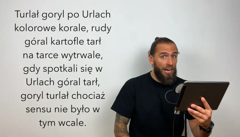 Mężczyzna z brodą i kitką czyta tekst o japońskich łamańcach językowych, gdzie goryl turlał się po Urlach, a góral tarł kartofle.