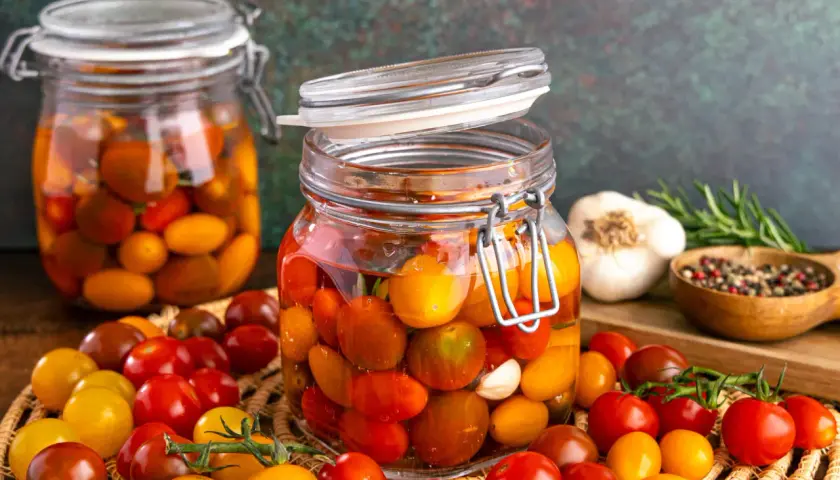 Gläser mit bunten Kirschtomaten, bereit zum **Tomaten fermentieren**. Daneben Knoblauch, Rosmarin und Pfefferkörner.