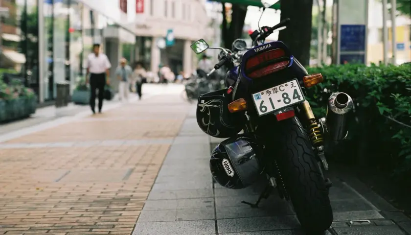 Una moto Yamaha aparcada en la acera, con dos cascos colgados. Al fondo, gente pasea por la calle.