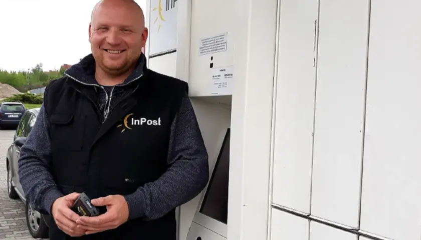 Uśmiechnięty kurier InPost trzyma skaner. Zastanawiasz się, ile zarabia kurier InPost?