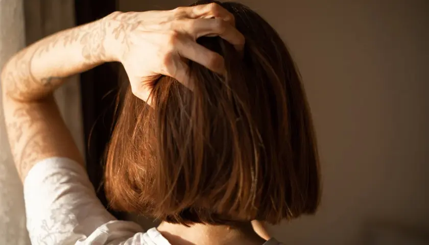 Dłoń przeczesuje cienkie włosy w stylu blunt bob. Cień koronki na ramieniu dodaje uroku.