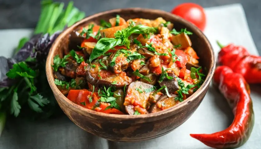 A miseczce caponata siciliana, pełna bakłażana, pomidorów i papryki, ozdobiona świeżą bazylią i pietruszką.