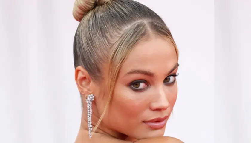 Elegancka kobieta z blond włosami spiętymi w wysoki kok. Jej **ulizane włosy** idealnie podkreślają rysy twarzy i błyszczące kolczyki.