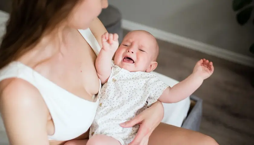 Bambino piange per la dentizione neonato rimedi. Mamma lo culla, cercando sollievo.