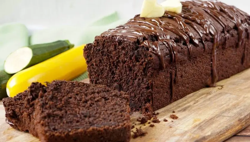 Saftiger Zucchini Schoko Kuchen, mit Schokoladenglasur und Herz-Dekoration, daneben Zucchini und gelbe Zucchini.