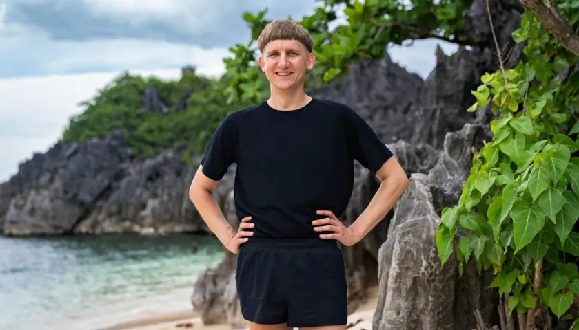 Pål Robinson står på en strand med klippor och grönska bakom sig.