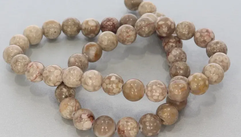 Zwei Stränge mit runden, beige-braunen Korallenperlen, die die Bedeutung von Schutz und Heilung symbolisieren.