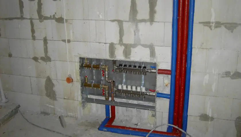 Instalacja hydrauliczna przed tynkami: widoczny rozdzielacz ogrzewania podłogowego i rury w ścianie z bloczków.