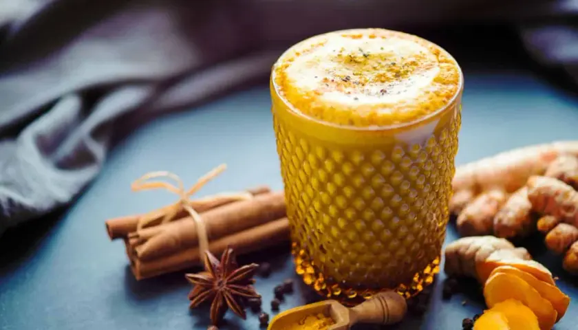 Ein Glas goldener Kurkuma Kaffee, verziert mit Zimtstangen, Sternanis und frischer Kurkuma.