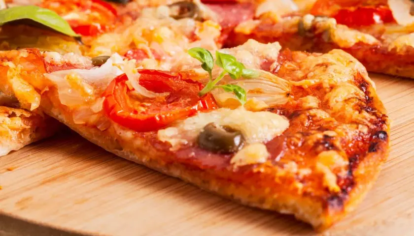 Pyszna pizza na serku wiejskim z pomidorami, oliwkami i bazylią, podana na drewnianej desce.