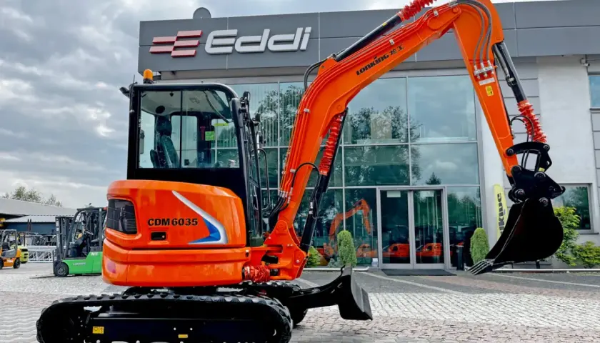 Pomarańczowa koparka gąsienicowa CDM 6035 przed budynkiem z logo Eddi.