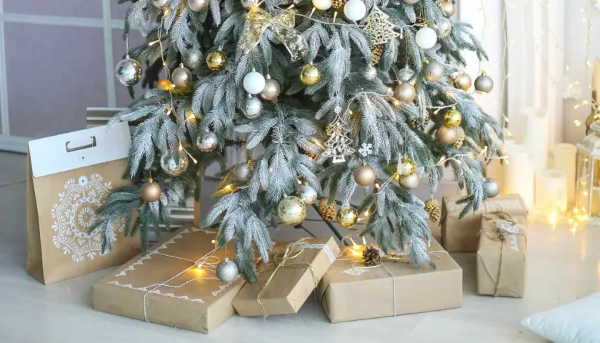 A frosted Christmas tree with gold and silver ornaments, fairy lights, and gifts wrapped in brown paper. Perfect christmas tree decor inspo for a cozy holiday.