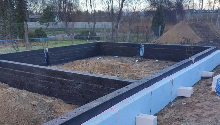 Budowa domu w toku. Widoczne fundamenty z bloczków betonowych i styropianu, przygotowane do dalszych prac.