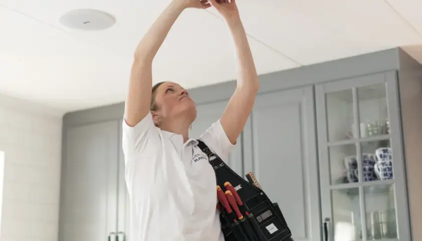 En elektriker med verktyg i bältet installerar en ojordad lampa i taket.
