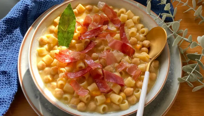 Un piatto fumante di pasta e ceci, arricchito da fette di prosciutto crudo e una foglia di alloro.
