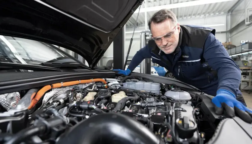 Mecánico con gafas de seguridad revisa el motor de un coche para su mantenimiento anual.