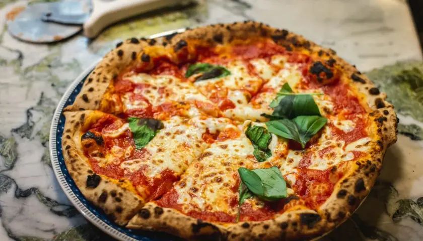 Pyszna pizza Margherita z bazylią na talerzu, obok nóż do pizzy.