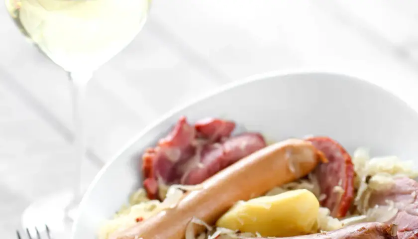 Un verre de vin blanc accompagne une choucroute de la mer généreuse avec saucisses et pommes de terre. Quel vin avec choucroute de la mer ?