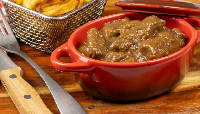 Un plat de carbonade flamande mijotée dans une cocotte rouge, accompagné de frites dorées dans un panier métallique. Un délice réconfortant.