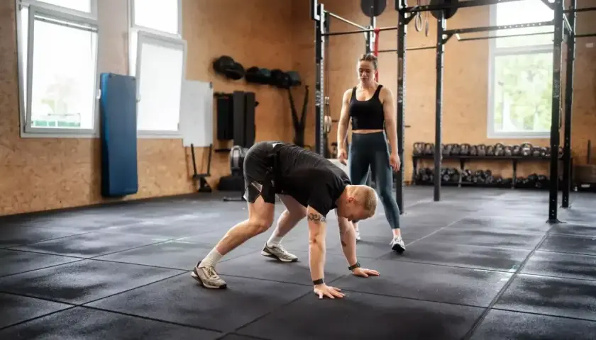 Trenerka obserwuje mężczyznę wykonującego burpee, ćwiczenie znane z intensywności.