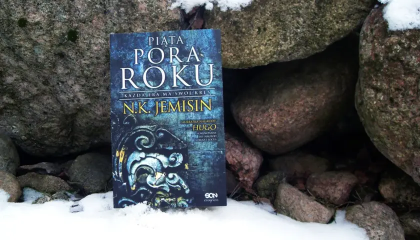 Książka "Piąta pora roku" N.K. Jemisin leży w śniegu między kamieniami. To opowieść o końcu świata, który przychodzi jak piąta pora roku.