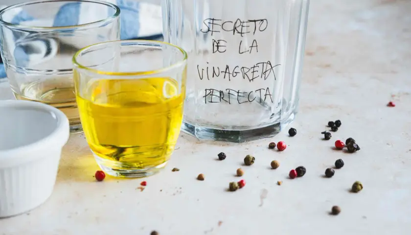 Ingredientes para la receta de vinagreta perfecta: aceite, vinagre y granos de pimienta.