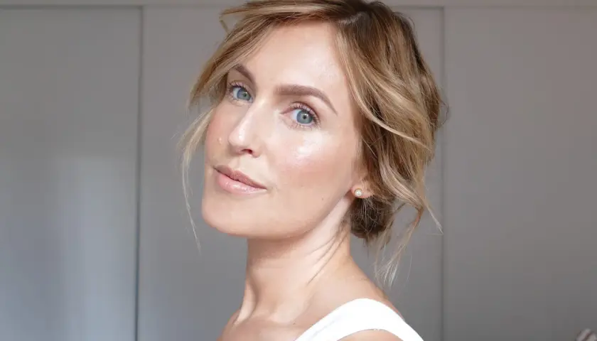 En kvinna med blå ögon och blont hår visar hur man får glow i ansiktet med naturlig makeup och lyster.