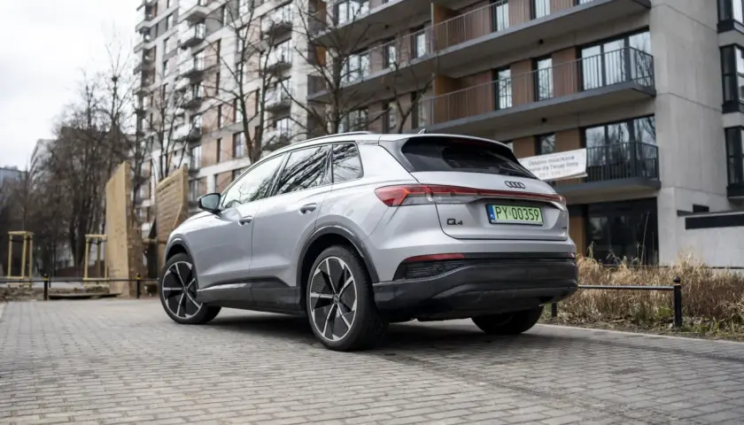 Srebrny Audi Q4 elektryk z zieloną tablicą rejestracyjną stoi na brukowanym podjeździe przed nowoczesnym budynkiem mieszkalnym.