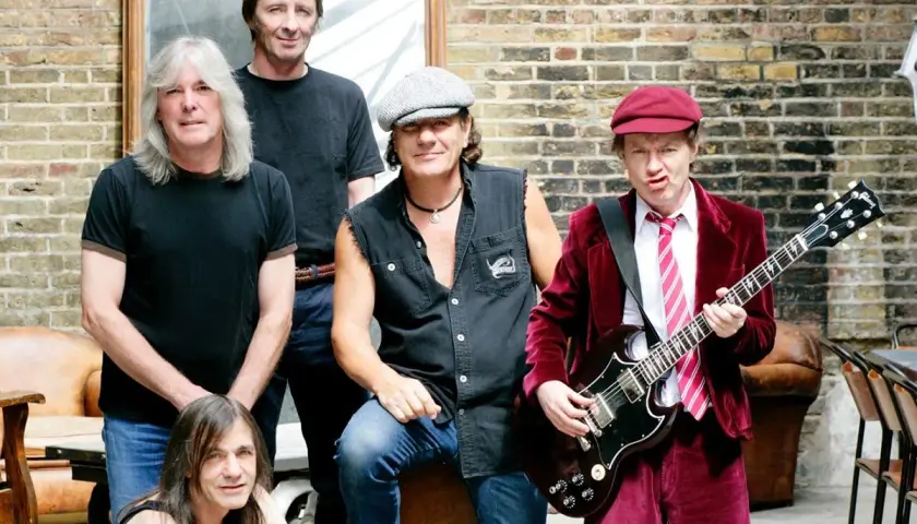 Zespół AC/DC w komplecie, gotowy do rock and rolla. Angus Young z gitarą, Brian Johnson w kultowym stroju.